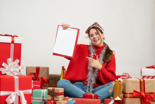 礼物圣诞快乐的女孩戴着圣诞帽拿着纸围坐在白色的礼物上座位女孩成人