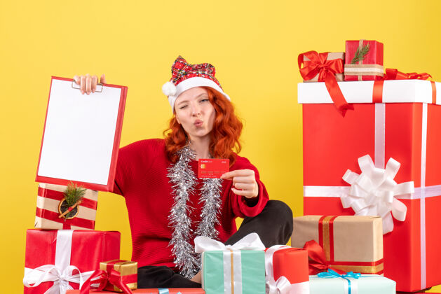 女性年轻女子围坐在圣诞礼物前 手持银行卡在黄色的墙上礼物抱着情感