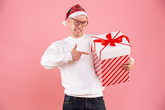 男性一个年轻人拿着大礼物在粉红色墙上的前视图举行年轻礼品盒