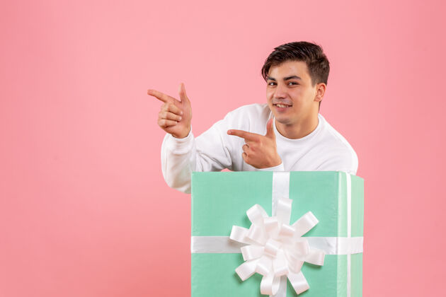 盒子隐藏在粉红色墙上的礼物里面的年轻人的正面视图高尔夫球手微笑微笑