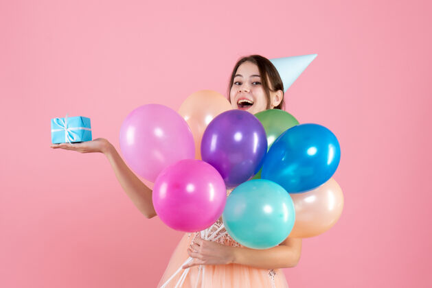 乐趣戴着派对帽的派对女孩手里拿着五颜六色的气球和粉色的礼物举行生日气球
