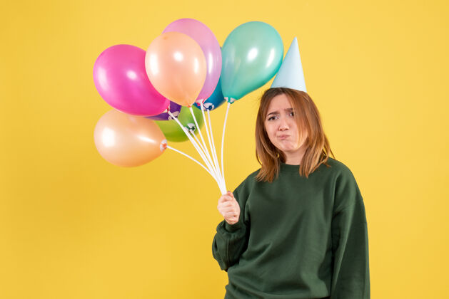 女性正面图：带着彩色气球的年轻女性庆祝颜色吹