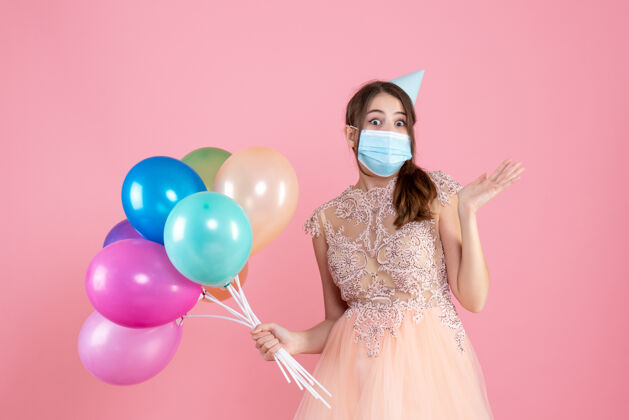 气球戴着派对帽和医用面具的神奇女孩手里拿着粉色的彩色气球医疗庆祝聚会