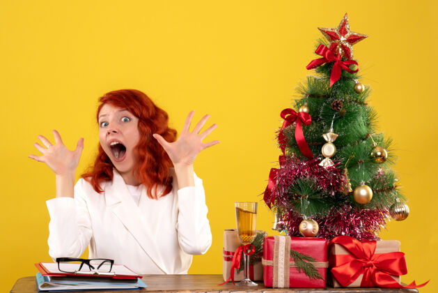 女女工人坐在桌子后面 手里拿着圣诞礼物和黄色的圣诞树圣诞节礼物坐着