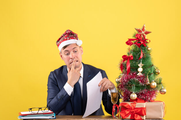 行政人员焦躁不安的男人坐在圣诞树旁的桌子前 黄色的墙上摆着礼物商务会议礼物