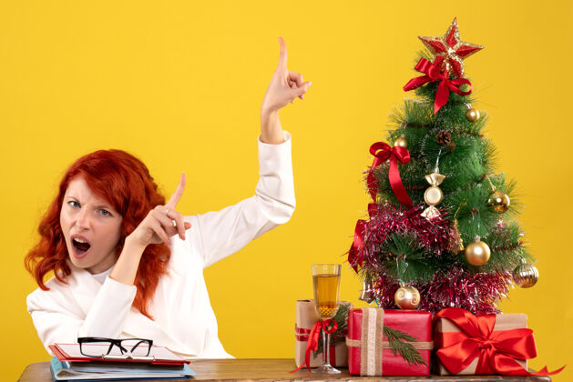 女工人女工人坐在桌子后面 黄色桌子上放着圣诞礼物和圣诞树工人坐着礼物