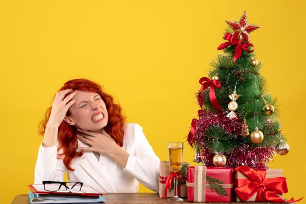 女女工人坐在桌子后面 手里拿着圣诞礼物和黄色的圣诞树桌子树工人
