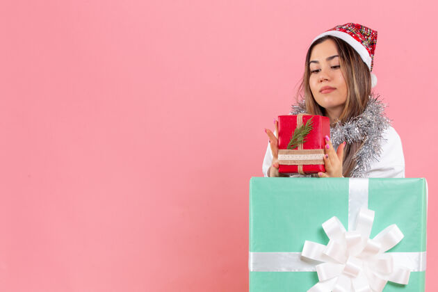 前面里面的年轻女子正拿着另一件礼物在粉红色的墙上圣诞节圣诞快乐人