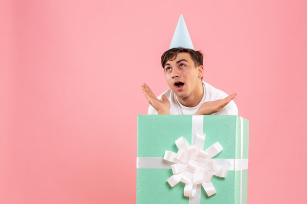 男性一个年轻人躲在粉红色的墙上礼物的正面视图丝带庆祝盒子