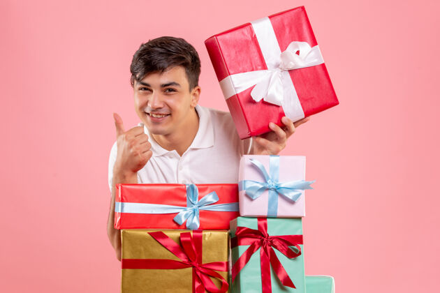 年轻粉红色墙上的圣诞礼物周围的年轻人的正面视图礼物年轻男性快乐