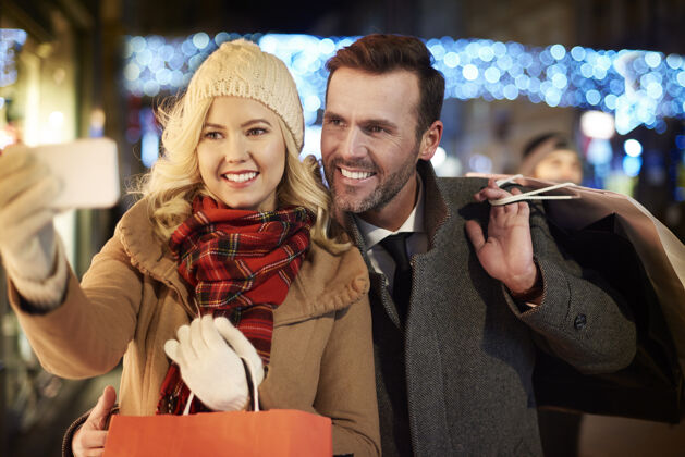 购物女人在购物时快速拍照圣诞灯男人温暖