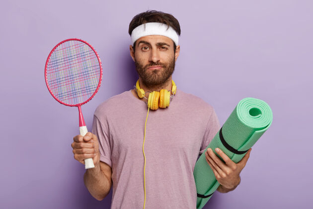 困惑一个严肃的男人准备在消遣时打网球 拿着球拍和卡雷马特 听音乐的孤立镜头强壮健康感觉