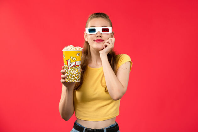 电影正面图：年轻女性手持爆米花套装 戴着d型太阳镜 坐在浅红的办公桌上 看电影 看电影 看女孩电影漂亮剧院爆米花