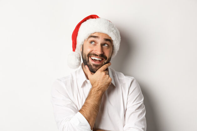 西装派对 寒假和庆祝概念特写的快乐男人计划圣诞礼物清单 戴着圣诞帽 看着左上角若有所思开朗节日庆祝