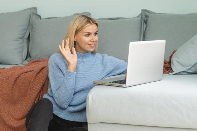 社会距离大流行期间 一个女人在家里用笔记本电脑打视频电话并挥手致意女性冠状病毒预防