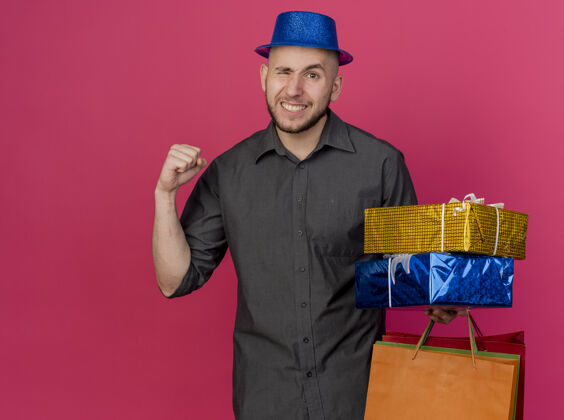 礼品盒自信的年轻英俊的斯拉夫党人戴着党的帽子拿着礼包和纸袋包盒子拿着