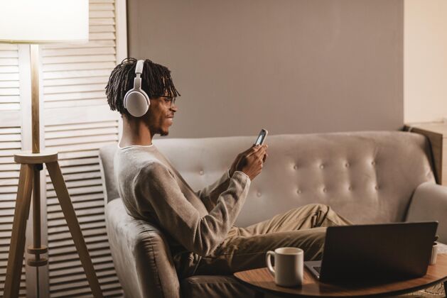 电子产品坐在沙发上使用智能手机和耳机的男人的侧视图科技人水平