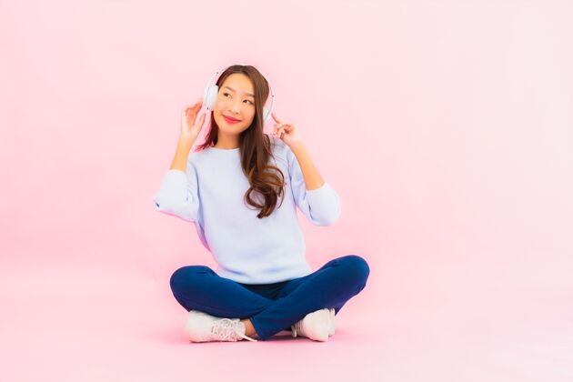 旋律肖像美丽的亚洲年轻女子用智能手机和耳机在粉红色的墙上听音乐音乐美丽休闲