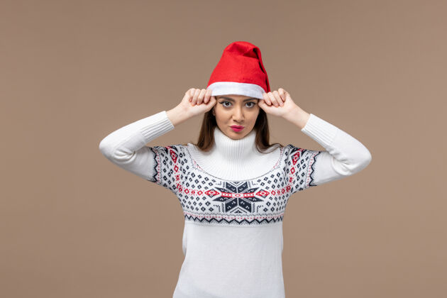 年轻前视图年轻女性戴着深棕色背景的红色圣诞帽 感受着圣诞节的节日气氛人物年轻女性帽子