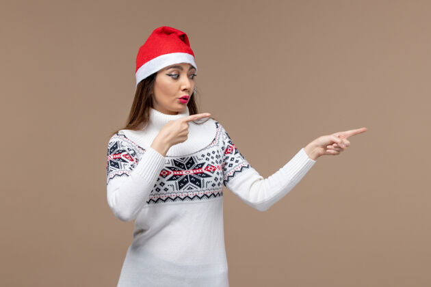女性正面图年轻女性在棕色背景上戴着红帽子摆姿势感慨圣诞新年新年份肖像