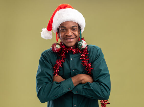 帽子快乐的非洲裔美国人戴着圣诞帽 戴着花环 耳朵上戴着圣诞球 看着绿色背景下的摄像机 他玩得很开心快乐非洲耳朵