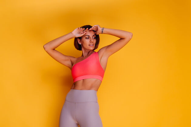 健康年轻健壮的女人穿着运动服 时髦的上衣和紧身裤 对着黄色的墙壁摆姿势人活跃积极