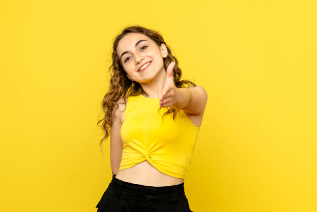 成人年轻女子在黄色墙上微笑的正面图可爱上衣肖像