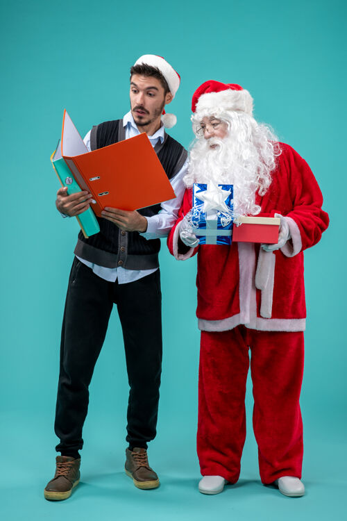 假期圣诞老人与年轻男性和礼物在蓝色墙上的正面视图庆祝男人人