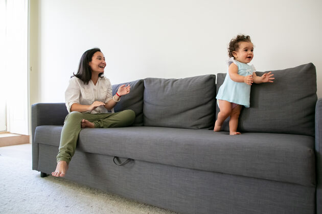 可爱快乐的妈妈看着小女孩在沙发上迈出第一步全长父母和童年的概念走路小女人