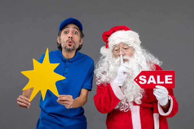 男人圣诞老人的正面图 男性信使手持销售横幅 灰色墙上有黄色标志帽子快乐快递