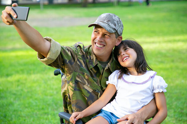 手机快乐的残疾军人爸爸和他的小女儿一起在公园里自拍女孩坐在爸爸的大腿上退伍军人或残疾概念采取成人射击