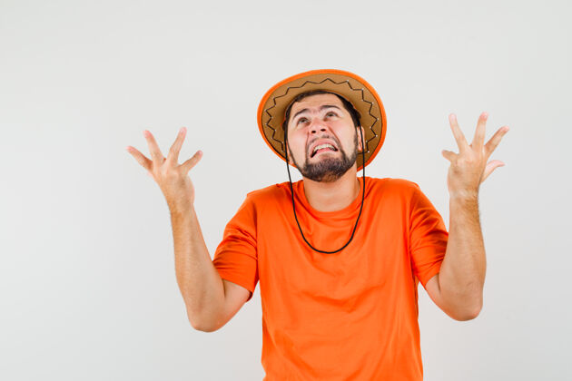 男人身穿橙色t恤 戴着帽子的年轻人以困惑的姿势举手致哀正视图模特人男性