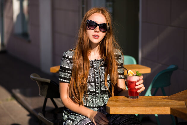 豪华一位留着长发 笑容迷人的时尚年轻女子 手里拿着美味甜美的夏日鸡尾酒柠檬水城市坐着头发