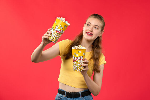 灯光正面图年轻女性在电影院拿着爆米花包在浅红墙电影院里看女性趣味电影电影成人漂亮