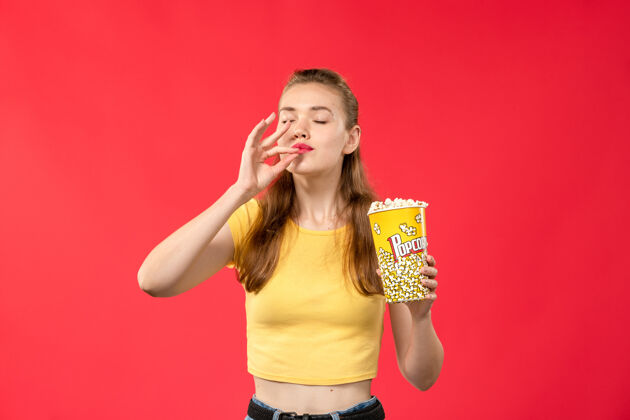 年轻前视图年轻女性在电影院拿着爆米花包在浅红色的墙上看电影电影电影院电影
