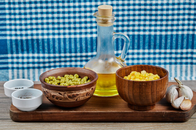 蓝色用桌布把煮好的甜玉米和青豆 香料 油和蔬菜放在木板上玉米大蒜罐装