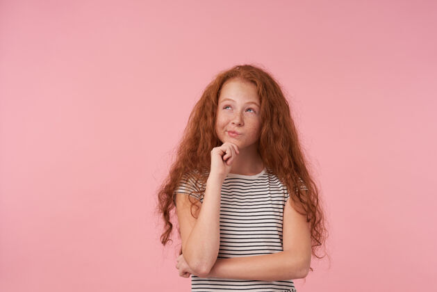 发型可爱的红发卷发女孩的肖像 随意的发型摆在粉色背景上 手放在下巴上 梦幻般地向上看 穿着条纹连衣裙头发下巴女学生