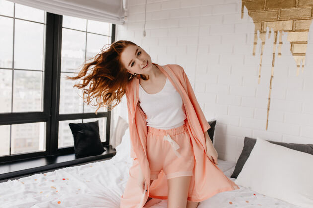 红发快乐的微笑女孩在床上摆姿势可爱的欧洲女模特穿着睡衣在早晨放松休息休闲成人