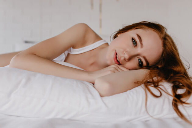成人迷人的红发女模特躺在枕头上看室内照片 快乐的姜黄色卷发美女笑休息室内