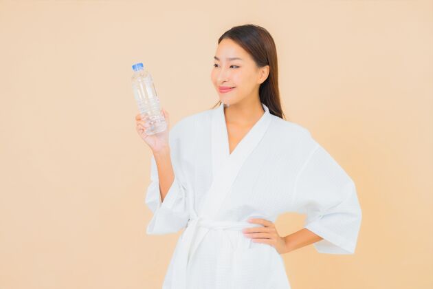 锻炼肖像美丽的亚洲年轻女子与瓶装水喝米色瓶子水瓶运动装