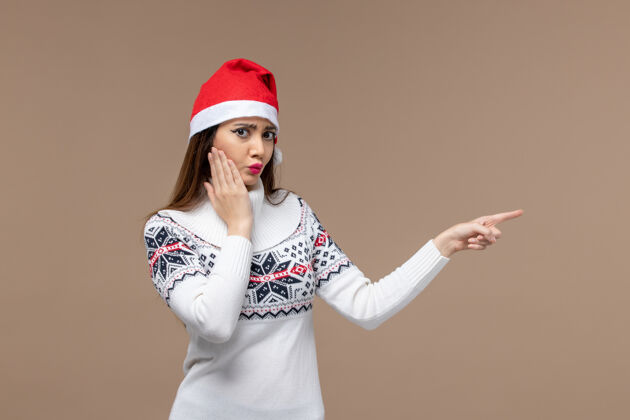 新正面图：年轻女性戴着红帽子在棕色桌子上摆姿势 感慨圣诞新年年份年轻微笑
