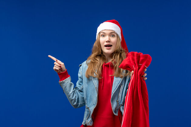 成人正面图蓝色地板上拿着礼物的年轻女性圣诞假期情感包前面表演者包