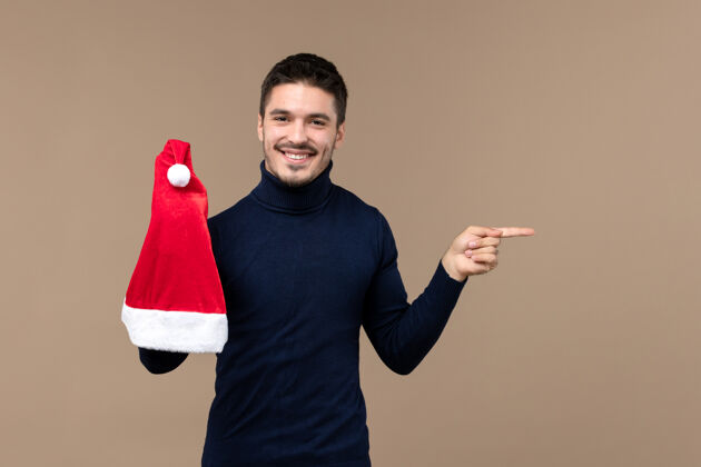 背景正面图：年轻男子在棕色背景上玩红帽 感慨圣诞新年手指情感圣诞节