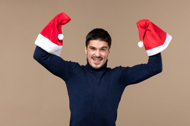 快乐正面图：圣诞假期 棕色背景上戴着红色帽子的年轻男性在活动男人棕色红色