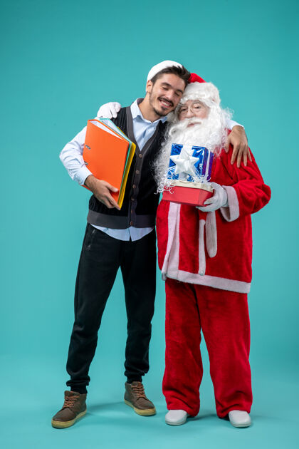 快乐圣诞老人与年轻男性和礼物在蓝色墙上的正面视图快乐圣诞老人礼物