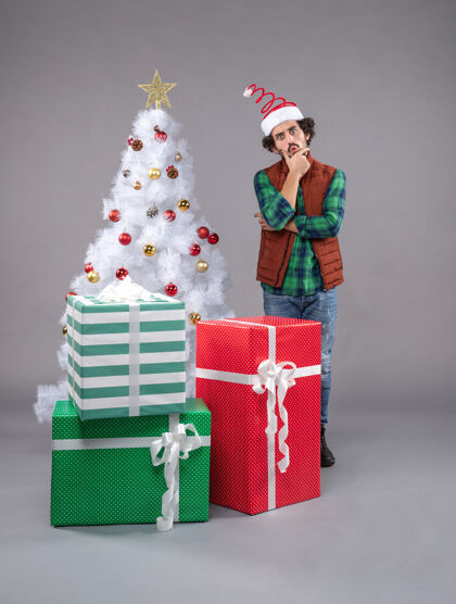 灰色年轻的男性在灰色的节日礼物年轻购物圣诞树