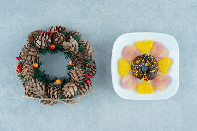 圆锥体在大理石上的松果花环旁边放着一盘marmelades和一个甜甜圈景观Marmelade甜点