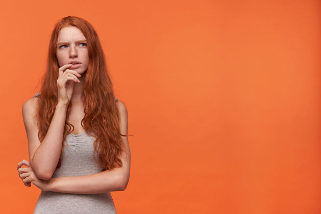 脸摄影棚拍摄的年轻迷人的红发女性 穿着休闲服 站在橙色背景下 手托下巴 沉思地向一边望去 试图收集思想沉思发型女性