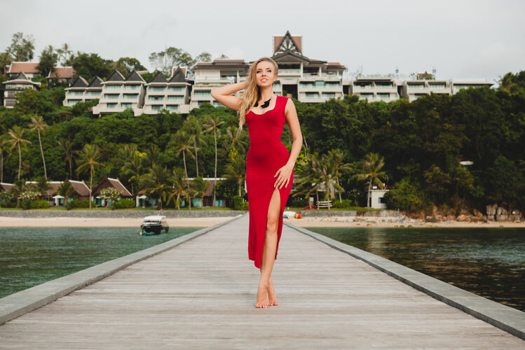 挥舞年轻漂亮迷人的女人独自站在豪华度假酒店的码头上 暑假 红色长裙 金色头发 性感服装 热带沙滩 诱惑 性感 微笑度假胜地优雅身体