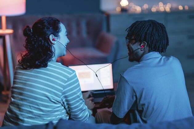 科技笑脸夫妇在家使用笔记本电脑和耳机的后视图人年轻现代